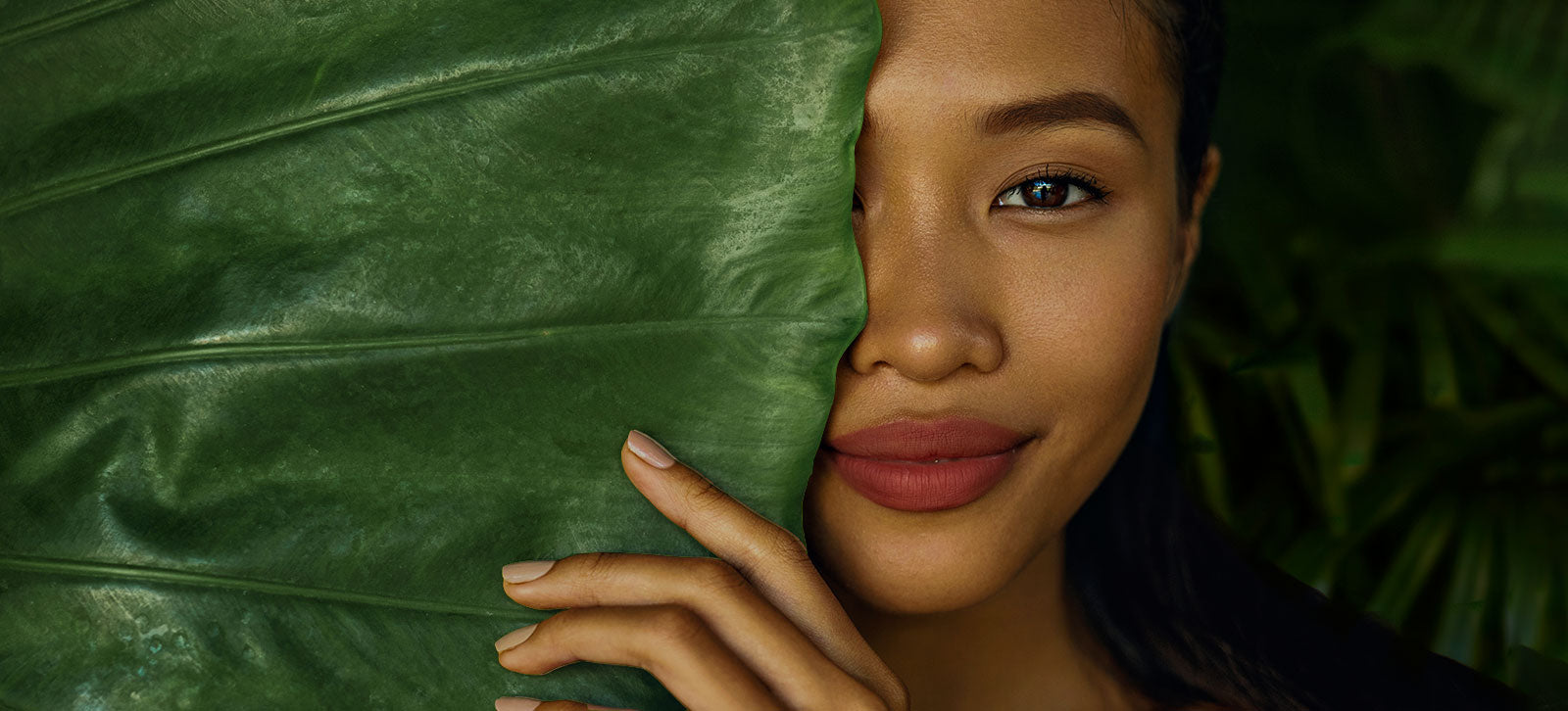 A woman smiling behind green leaves. 